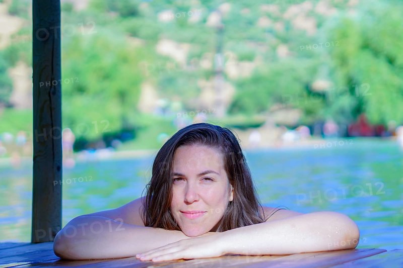 Beautiful brunette woman bathing in a lake perched on a wooden pontoon looking at the camera with a smile on her face