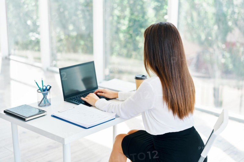 Back view of young businesswoman working with laptop in modern office