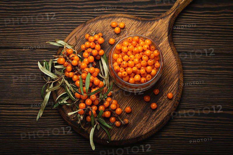 Sea buckthorn ripe berries in glass jar and branches with leaves top view on dark wooden rustic background, great for skin, heart, vessels and immune system, food photography, food photography