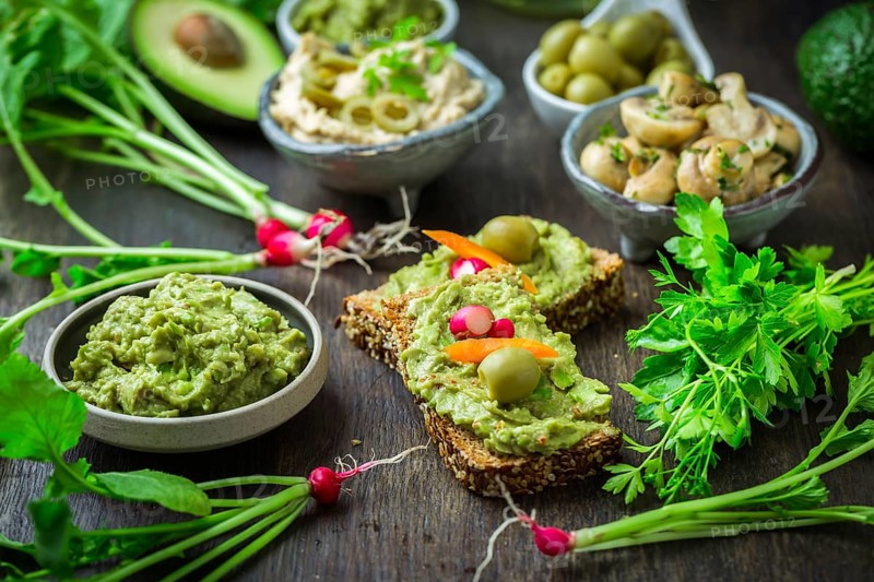 Wholemeal bread with avocado spread and vegetables on wooden kitchen table