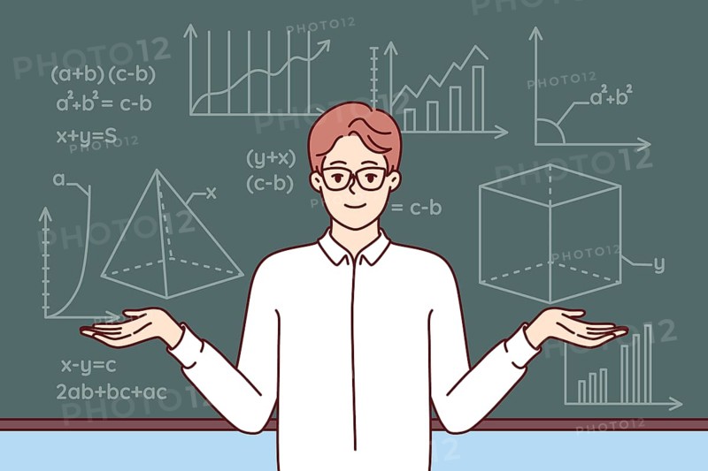Man mathematics teacher stands near school blackboard with formulas and geometric drawings. Young smart professor in white shirt and glasses works at university studying science of mathematics