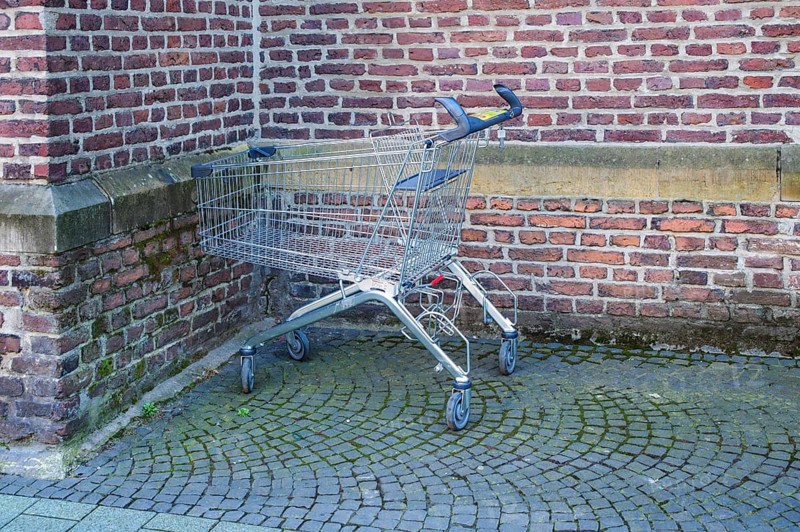 Metal shopping cart stands empty next to a brick wall on a cobblestone street, symbolizing consumerism, retail, and urban life, Bottrop, NRW, Germany, Europe