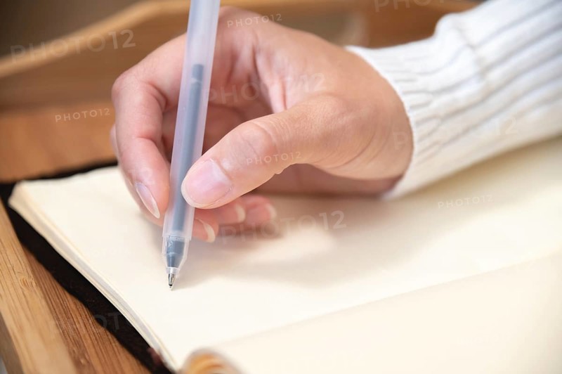 Close-up of female hands writing with gel black pen in leather notepad on wooden table at home