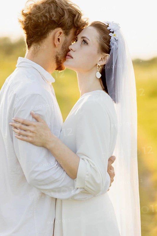 A couple sharing an affectionate moment outdoors in wedding attire, warm lighting
