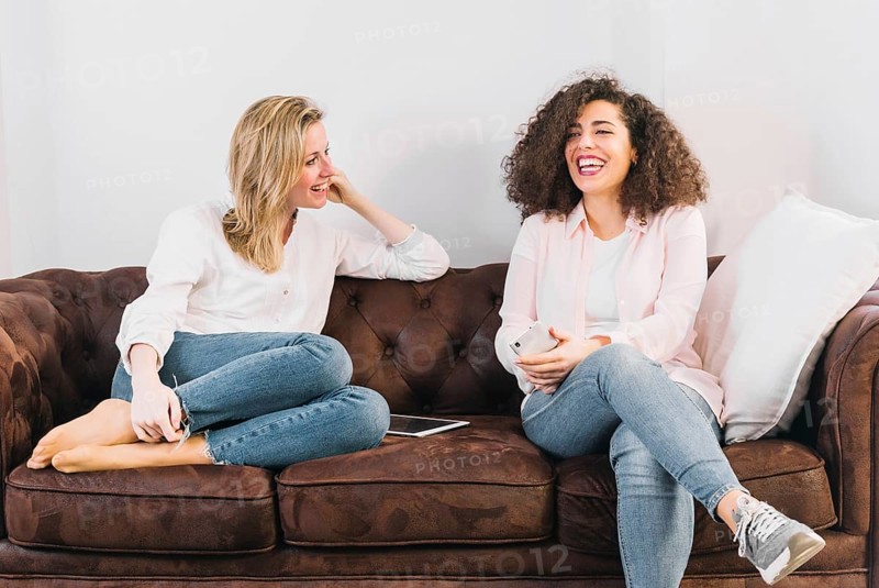 Cheerful women with technologies speaking sofa