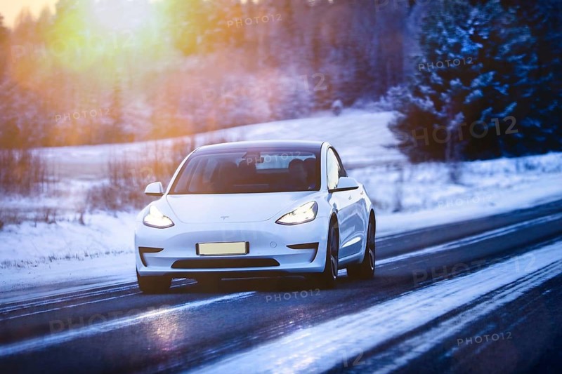 White Tesla Model 3 electric car at speed on highway in winter at dusk. Salo, Finland. December 27, 2021