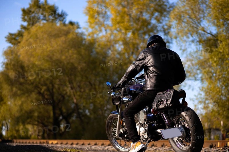 Male motorcyclist in a leather jacket and helmet on a vintage custom motorcycle in nature. Concept of motorcycle life and the beginning of the season