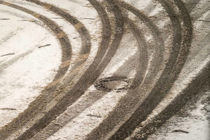 Car tire tracks curving on a snowy road surface in winter, indicating vehicle movement and winter driving conditions