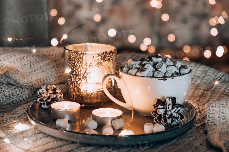 Cup with hot winter cacao and marshmallows on bed. Christmas lights. Pine cones decoration. Cozy winter days. Hygge