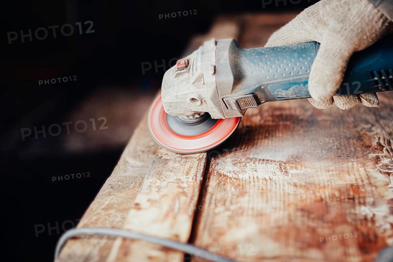 Close-up of an angle grinder being used on a wooden table by a gloved hand