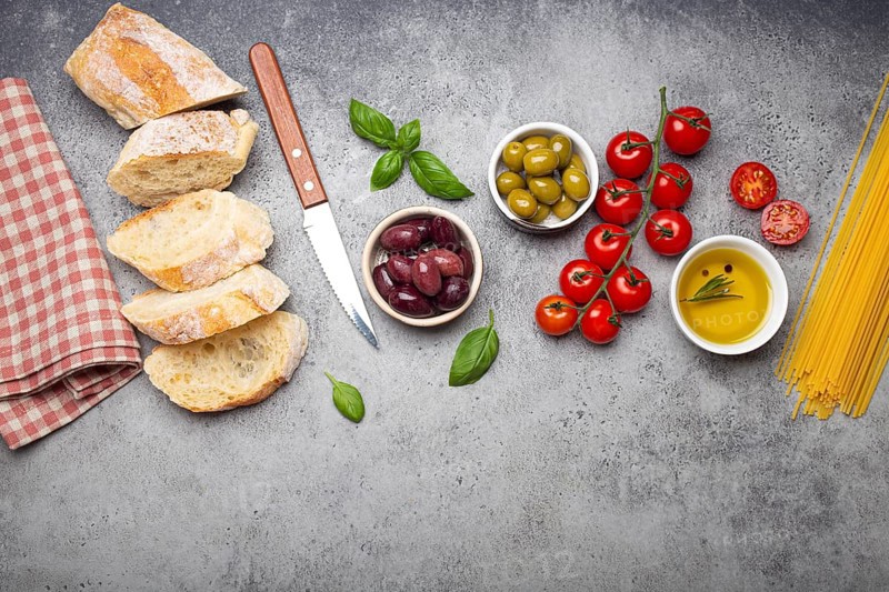 Food composition with sliced ciabatta, olives, olive oil, spaghetti, fresh basil, cherry tomatoes on gray concrete stone rustic background top view, copy space. Italian cuisine concept, food photography, food photography