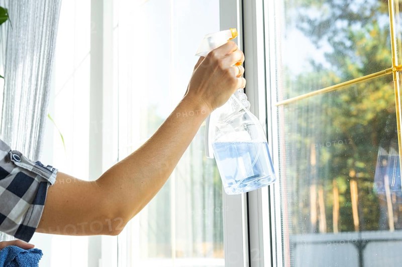 Woman manually washes the window of the house with a rag with spray cleaner and mop inside the interior with white curtains. Restoring order and cleanliness in the spring, cleaning servise