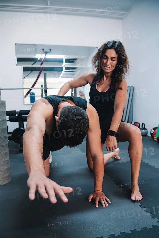 A personal trainer assists a man in a gym during a workout session, tarragona, spain