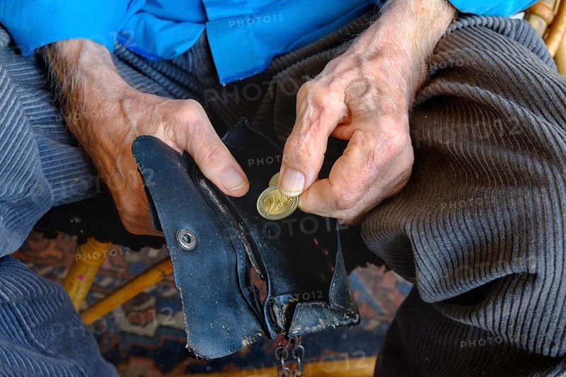 An old man takes a two euro coin from his worn wallet. Close-up, landscape format. An old man takes a two-euro coin out of his worn-out purse. Close up, horizontal format