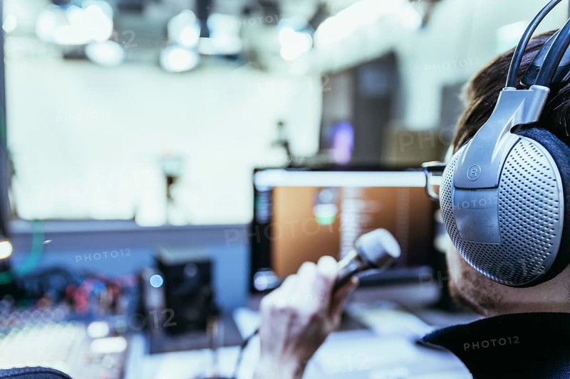 Young man is sitting in the recording studio and talks into the microphone, buttons and equipment in the blurry background
