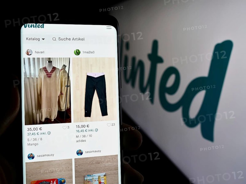Stuttgart, Germany, 03-17-2024: Person holding cellphone with webpage of online secondhand marketplace company Vinted in front of logo. Focus on center of phone display, Europe