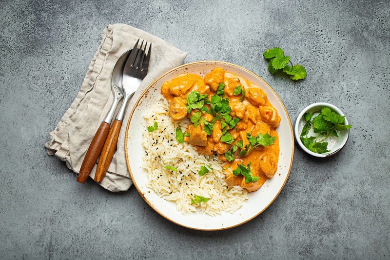 Traditional Indian dish chicken curry with basmati rice and fresh cilantro on rustic white plate on gray concrete table background from above. Indian dinner meal, food photography, food photography