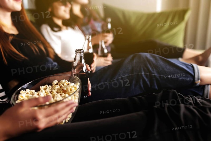 Friend group of people in 3D glasses are watching a movie, smiling, laughing. Eating and drinking while watching a movie in the cinema. Girls eat popcorn and drink soda in glass bottles. Relaxing time