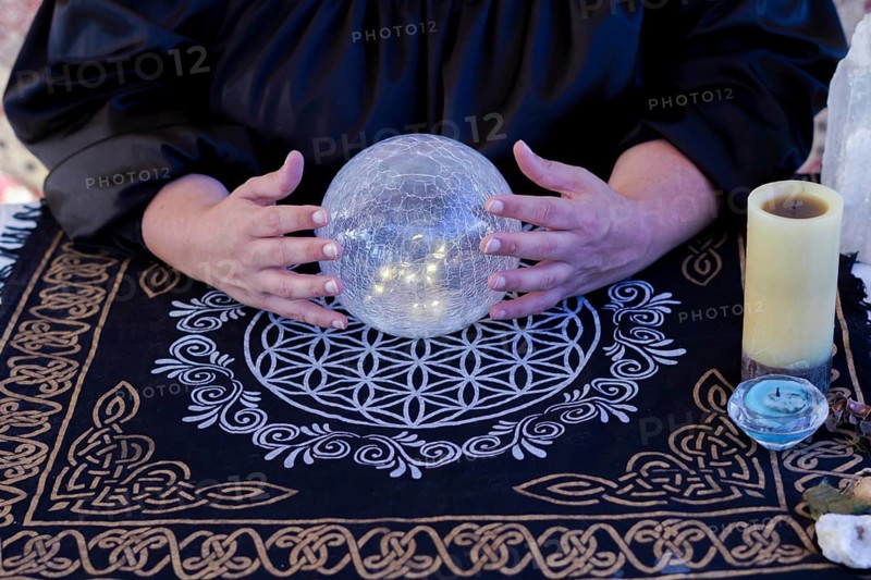Close up of a woman fortune teller dressed in black reads the future in a crystal ball
