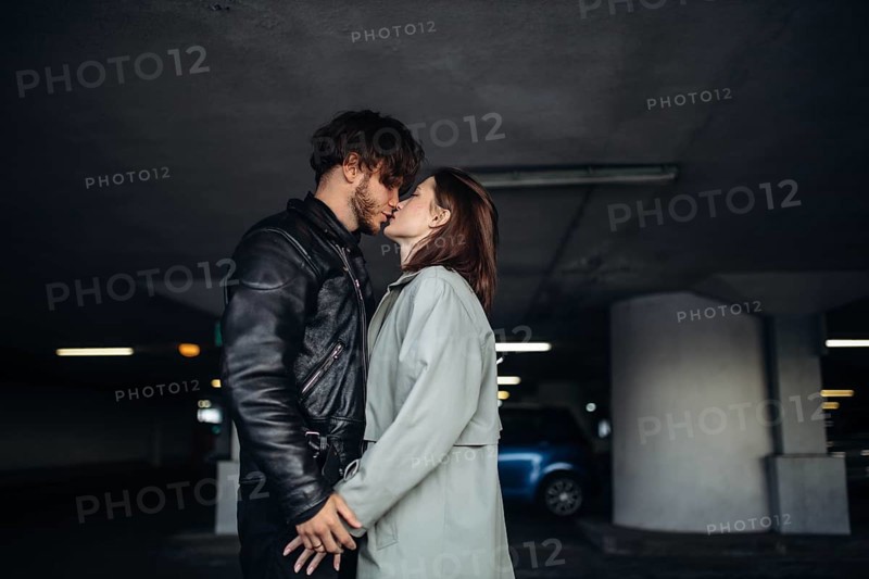 The couple shares a kiss in a dimly lit parking garage, showing intimacy and connection