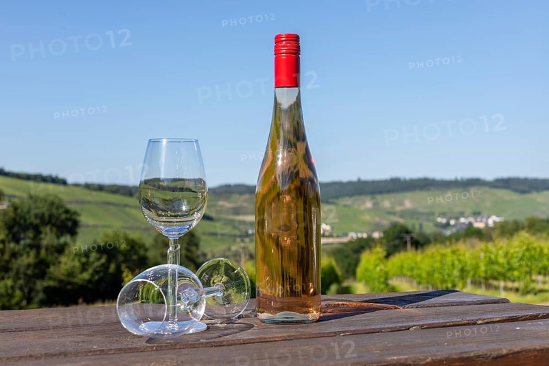 Wine bottle with glasses on wooden table with landscape on river moselle in background