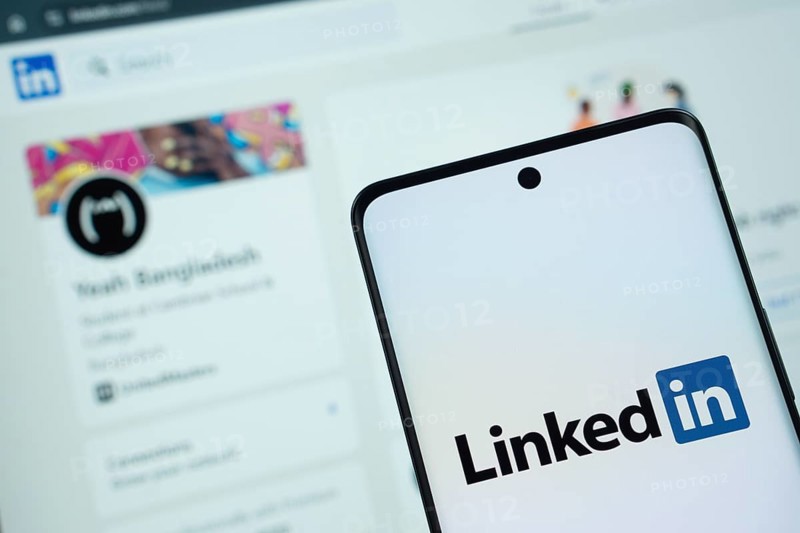 Dhaka, Bangladesh - 17 March 2025: The logo of the linked in is displayed on a smartphone screen, and the website linked in is visible on a computer screen in the background