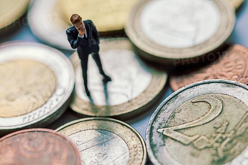 Figure of a thoughtful businessman between euro coins, studio shot, Germany, Europe