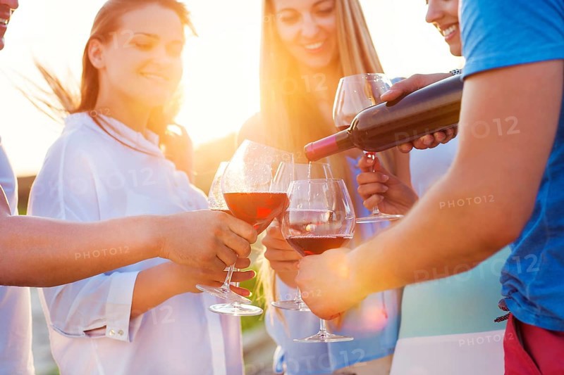 Group of happy friends having red wine on the beach. Sunset beach party
