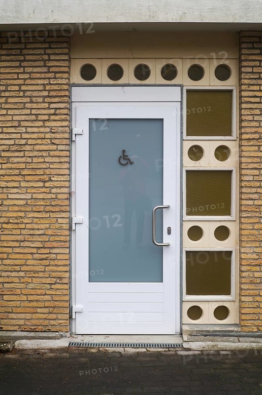 Public restroom door with accessibility sign for disabled people featuring frosted glass and white frame