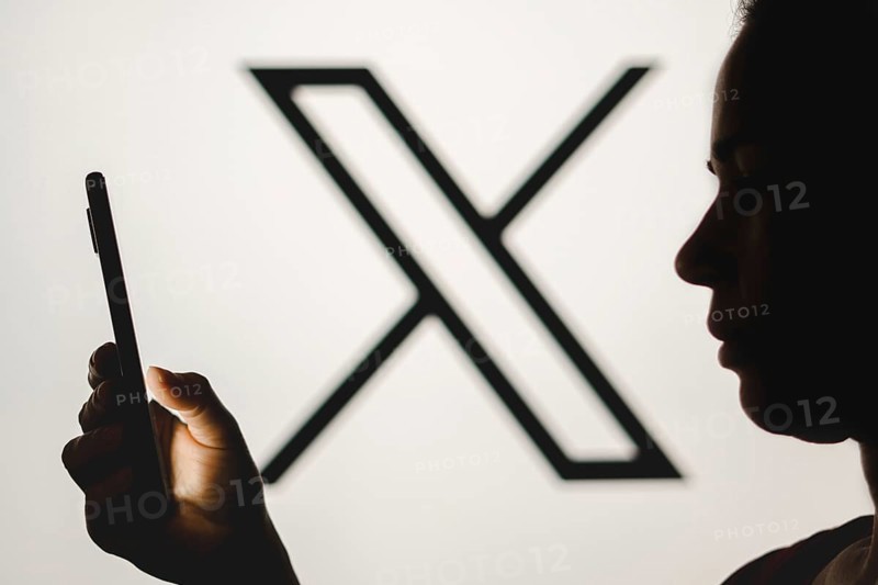 In this photo illustration, a woman's silhouette holds a smartphone with the Twitter (X) new logo in the background