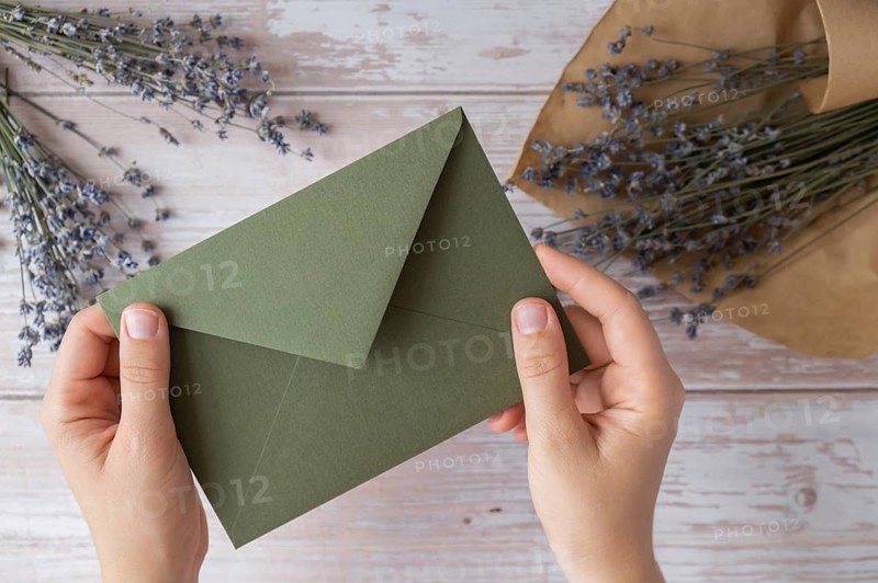 Flat lay composition of female hands holding green envelope with dry lavender flowers. Copy space template mock up. Top view. Concept of Wedding invitation postcard. Business advertisement brand blank
