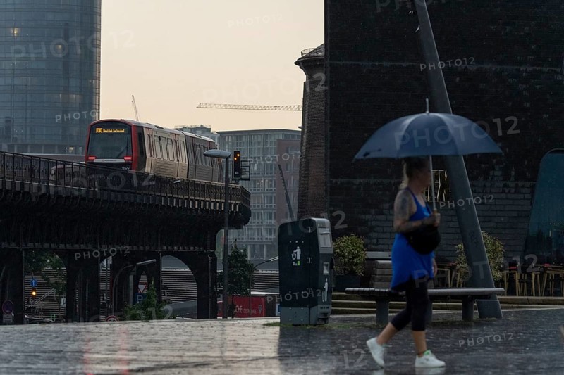 Symbolic picture weather, heavy rain in summer, thunderstorm, storm, tourist with umbrella on the way in the rain next to the underground line U3 at the Landungsbrücken in the harbour of Hamburg, Germany, Europe