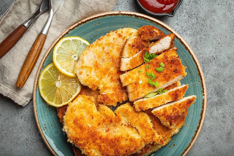 Crispy panko breaded fried chicken fillet with green salad and lemon cut on plate on gray rustic concrete background table with ketchup from above. Japanese style deep fried coated chicken breasts, food photography, food photography