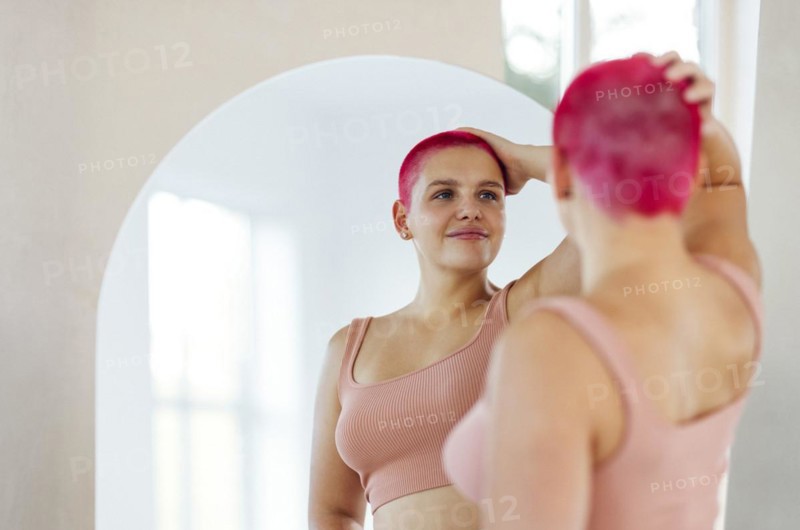Beautiful relaxed woman in sport clothes red shot hair looking to the mirror. Concept of body positive