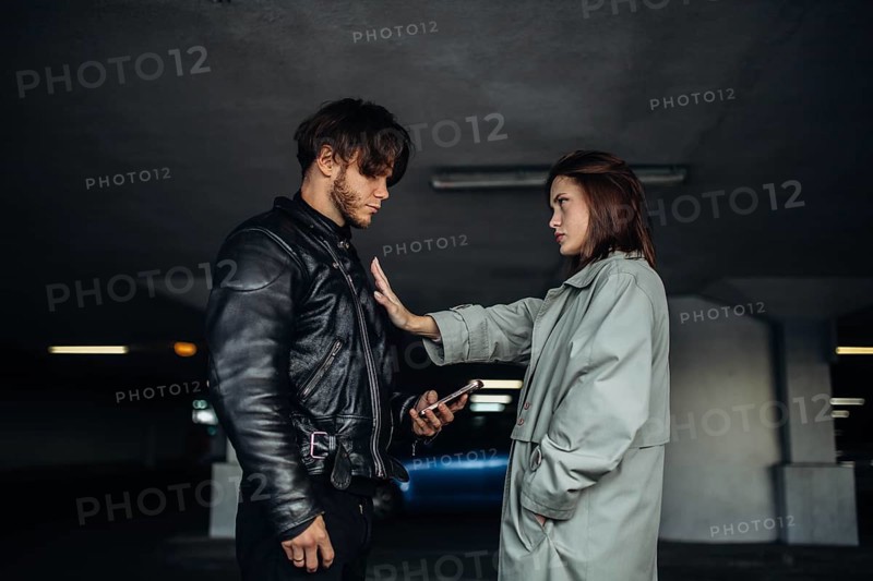A man and woman face each other in an underground parking garage, the atmosphere tense