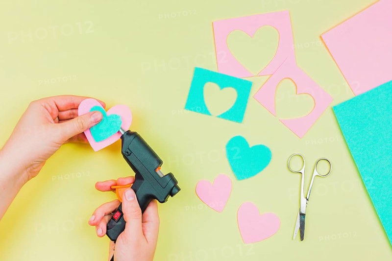 Close up woman s hand sticking paper heart shape with electric hot glue gun