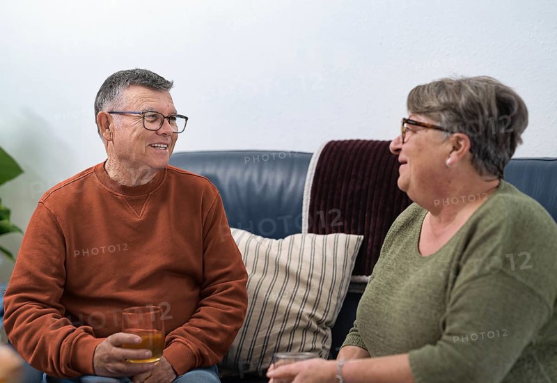 Happy retired couple enjoying a relaxing afternoon at home, sharing stories and drinks on a comfortable sofa, representing a healthy and fulfilling retirement