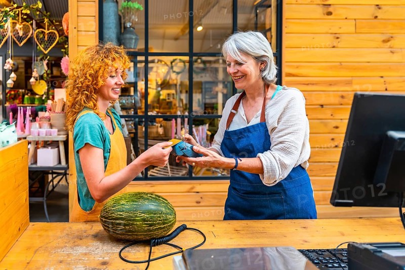 Happy customer paying with contactless credit card for a melon at a flower shop counter, small business and electronic payment concept