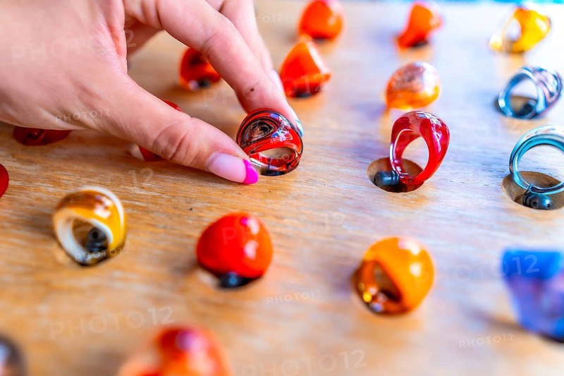 Woman's hand with pink nail polish picking up a colorful resin ring from a wooden display at a craft market