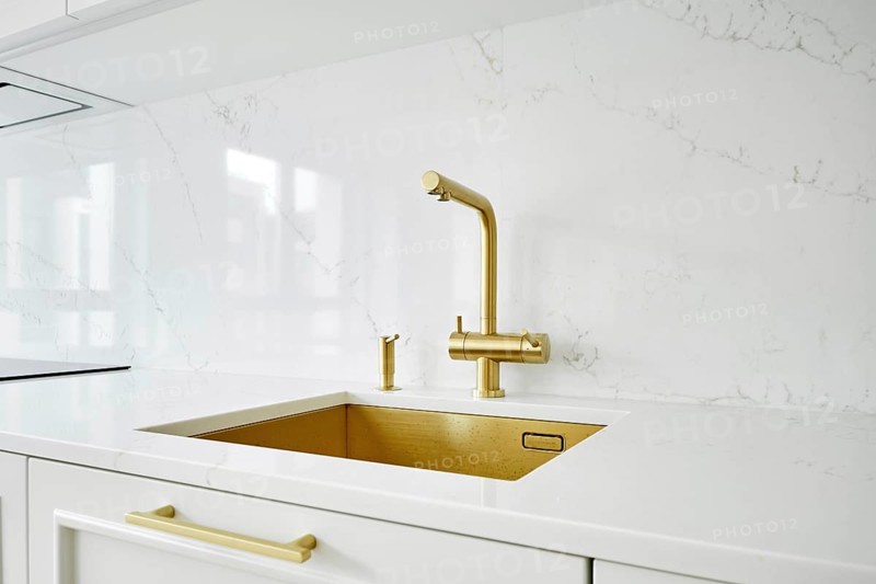Golden kitchen faucet and soap dispenser over a rectangular sink installed in natural stone countertop