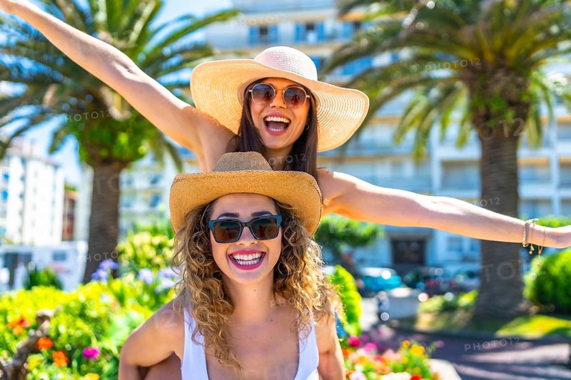 Two cheerful female friends are having fun during summer vacation, wearing sunglasses and straw hats