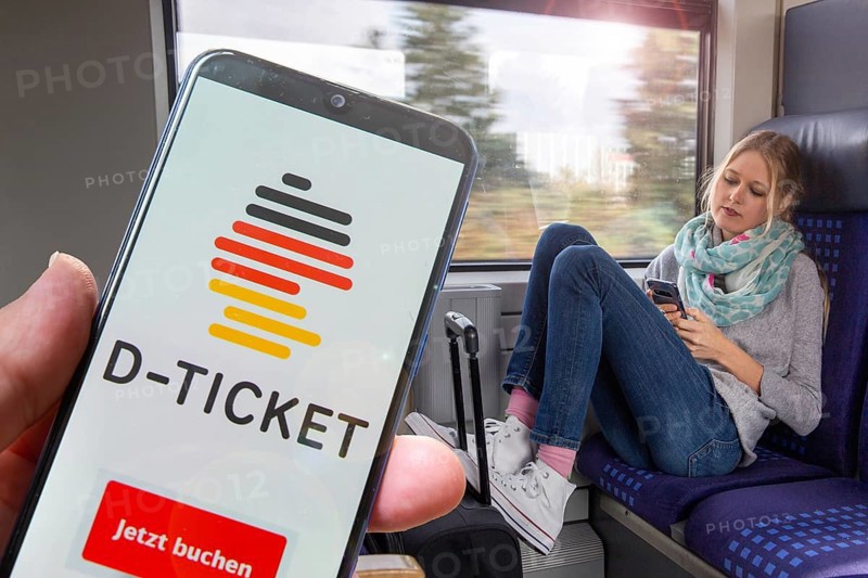 (Photomontage) Logo of the Deutschlandticket on the smartphone, in the background a young woman on the train