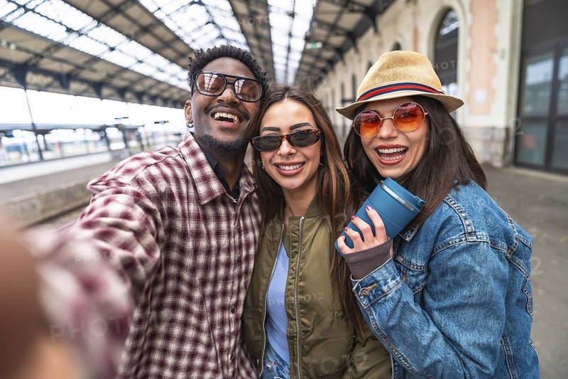 Three cheerful young tourists taking a selfie at the train station, excited for their upcoming travel adventure