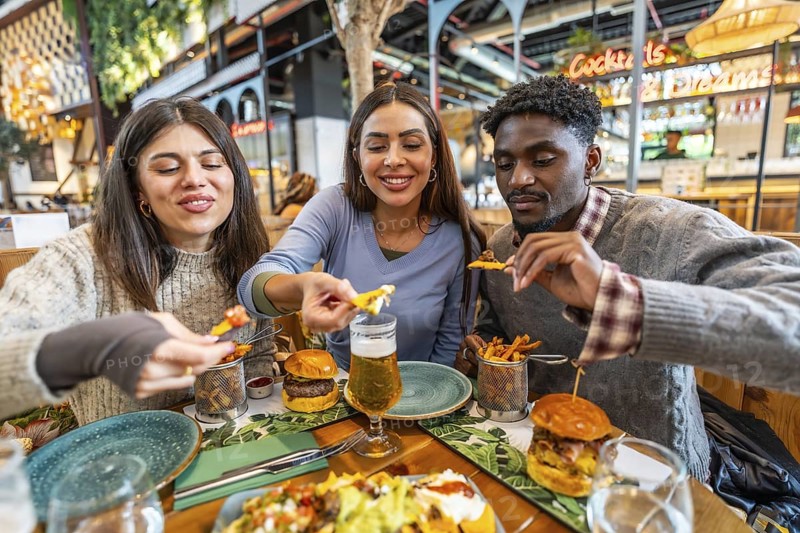Three happy friends enjoying a meal together, sharing nachos, burgers, and fries at a restaurant table
