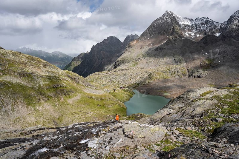 Mountaineer on a rocky hiking trail, view of the turquoise-blue mountain lake Großer Gradensee, behind her the summit of the Petzeck, Hoher Perschitzkopf and Kruckelkopf, Schober Group, Hohe Tauern National Park, Carinthia, Austria, Europe