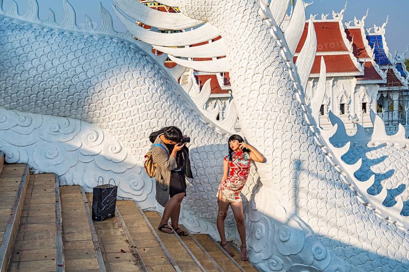 Photographer photographing young Thai woman on the steps of the Guan Yin (Goddess of Mercy) statue at Wat Huay Pla Kang Temple in Chiang Rai province of Northern Thailand