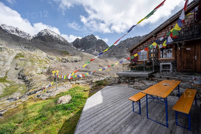 Colourful prayer flags, terrace at a mountain hut, mountain hut Adolf-Nossberger-Hütte, mountain landscape with rocky mountain peaks, in the background summit of Petzeck and Kruckelkopf, Schober group, Hohe Tauern National Park, Carinthia, Austria, Europe