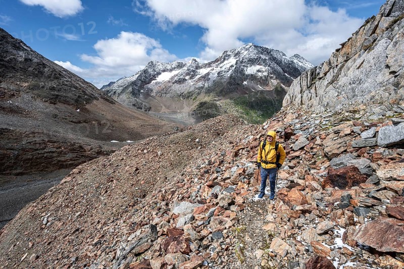Mountaineer on hiking trail in steep rocky mountain landscape with fresh snow in summer, behind mountain peak Roter Knopf, descent from the Hornscharte on the Wiener Höhenweg, Schober group, Hohe Tauern National Park, Carinthia, Austria, Europe