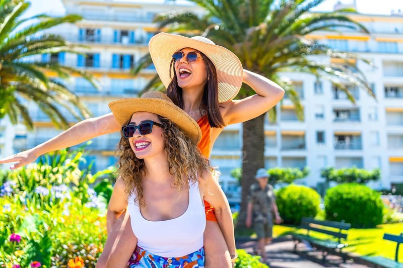 Two cheerful women wearing sunglasses and straw hats are having fun during their summer vacation in juan les pins, france