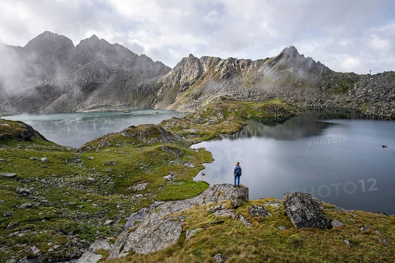 Mountaineer on a rock in front of mountain lakes Wangenitzsee and Kreuzsee, cloudy mountain peaks in the morning, Schober group, Hohe Tauern National Park, Carinthia, Austria, Europe